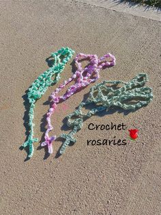 crochet rosarys laid out in the sand with flowers on top and bottom