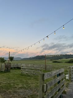 a fenced in area with lights strung over it and grass on the other side