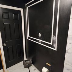 a bathroom with black walls and white trim on the door, toilet paper roll in front of it