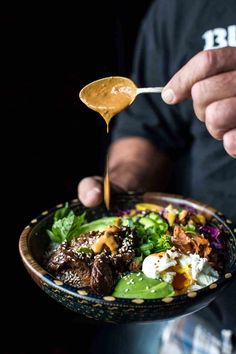 a person is holding a spoon over a bowl of food that includes meat, lettuce and eggs