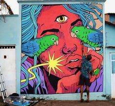 a man standing in front of a colorful painting on the side of a blue building