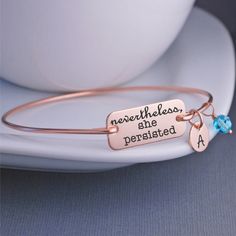 "A rectangle measuring 1 1/8 of an inch across is engraved with the words \"nevertheless, she persisted \". Each bangle is hand formed from heavy gauge wire and then hammered and tumbled for shine and strength. Available in 14k rose gold filled, 14k gold filled, and silver (sterling silver band with stainless steel disc). ALL Charms are optional! Make your metal and number of charms selection from the dropdown and then let me know the details in the text box! Available in these sizes (if you nee She Persisted, Nevertheless She Persisted, Graduation Gifts For Her, Text Box, Phoenix Az, Sterling Silver Bands, Silver Band, Graduation Gifts, Bangle Bracelet