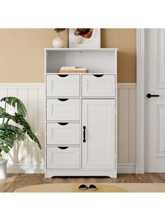 a white cabinet with four drawers and a mirror on the top shelf next to a potted plant