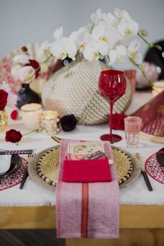 the table is set with red and gold plates, napkins, and wine glasses