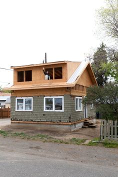 a house being built with wood shingles and windows on the roof, in front of a fenced yard