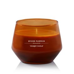 an orange glass candle sitting on top of a white surface with the words spiced pumpkin in