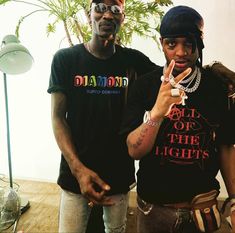 two young men standing next to each other in front of a plant and light fixture