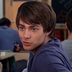 a young man sitting at a table with his hand on his chin looking into the camera