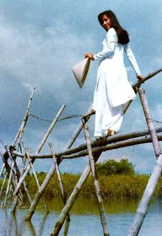 a woman standing on top of a wooden bridge in the middle of a body of water