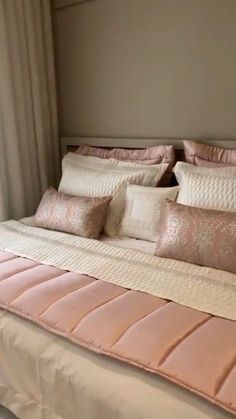 a bed with pink and white pillows on top of it in a bedroom next to a window