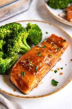 a plate with salmon and broccoli on it next to a container of sauce