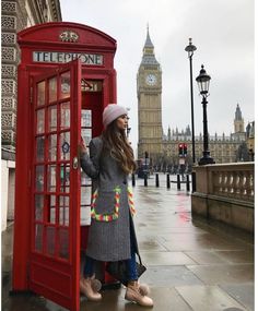 a woman standing next to a red phone booth