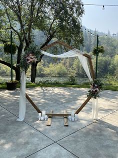 an outdoor wedding setup with white draping and flowers on the arbor, surrounded by greenery