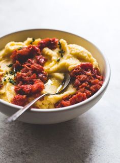 a white bowl filled with pasta and sauce on top of a marble counter next to a silver spoon