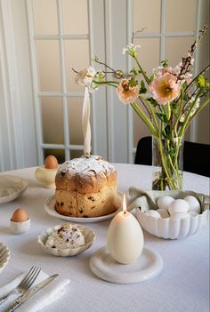 a table topped with cake and eggs next to a vase filled with flowers on top of a white table cloth