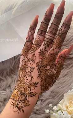 a woman's hand with henna tattoos on it and flowers in the background