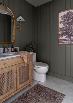 a white toilet sitting next to a bathroom sink under a large golden mirror on top of a wooden cabinet