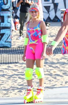 a woman riding a skateboard on top of a sandy beach next to another person