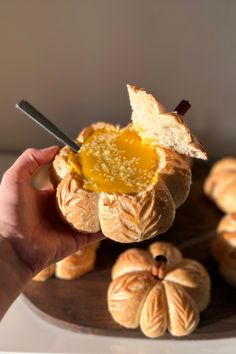 a person holding up a piece of bread with honey on it and other pastries in the background