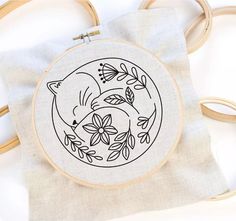 an embroidered hoop with a cat and flowers on it, next to a wooden frame