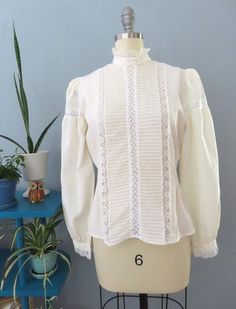 Vintage 80's Victorian blouse. Off white silk with high lace ruffle collar, eyelet lace, horizontal pleats and button lace cuffs. Button down back with billowy long sleeves with puffed shoulders. Sightly sheer overall. Straight hem. Gorgeous top would be great for a formal event.  Fits up to a size large. Please double-check the measurements below: MEASUREMENTS--Taken with garment laying flat, in inches, doubled: Bust: 40"  Waist: 38"  Shoulder: 14" Length: 23" {top neck to bottom hem} Neck: 14" Sleeve length: 24.5" Label/ Era: Royal Silk | 1980 Stated Size: 8 Fabric: Silk, acrylic buttons Condition: Excellent condition. Freshly laundered. No known issues.  ★ Shop entire shop here: https://www.etsy.com/shop/retrosuzysvintage Instagram | retrosuzysvintage Facebook | retrosuzysvintage Pinter Victorian Blouse, Lace Cuffs, Ruffle Collar, Eyelet Lace, Lace Ruffle, White Silk, Lace Blouse, Silk Blouse, Formal Event