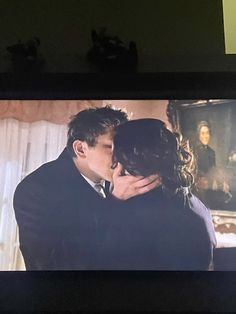 a man and woman are kissing in front of a tv screen with the image of a painting on it