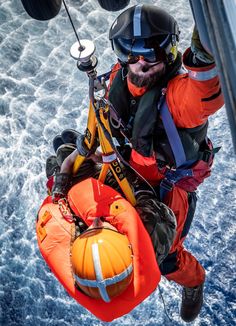 a man in an orange life jacket and safety gear hanging from the side of a boat