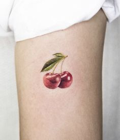 a small cherry tattoo on the side of a woman's thigh, with two cherries attached to it