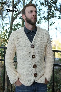 a man standing in front of a fence with his hands in his pockets, wearing a sweater and jeans