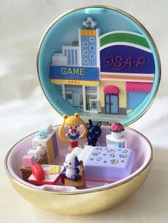 an open tin box with toys inside on a white tableclothed surface, in the shape of a toy store