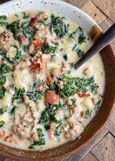 a bowl of soup with meat, spinach and cheese in it on a wooden table