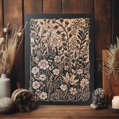 a black and white paper cut art piece sitting on top of a wooden table next to candles