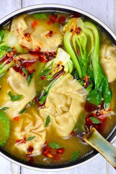 a pot filled with dumplings and vegetables on top of a wooden table next to a spoon