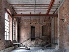 an empty room with brick walls and stairs in the center, surrounded by large windows