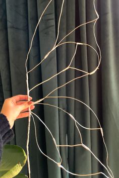 a person holding some kind of wire in front of a window with curtains behind them