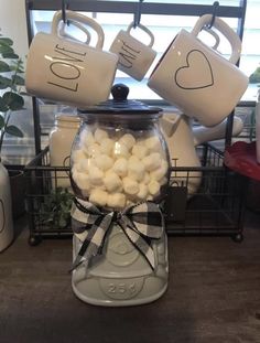 a jar filled with marshmallows sitting on top of a table next to two coffee mugs