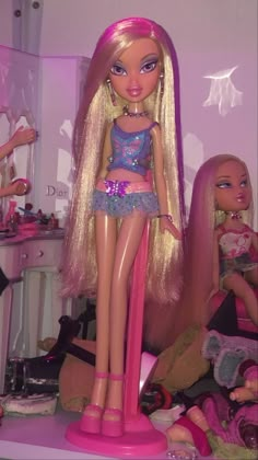 a barbie doll with blonde hair standing next to other dolls in a room full of toys