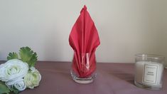 a red napkin sitting on top of a table next to a candle and some flowers