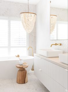 a white bathroom with two sinks and a bathtub in the middle, along with a chandelier hanging from the ceiling