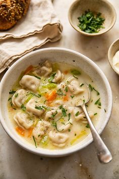 a white bowl filled with dumplings next to other bowls and bread on a table