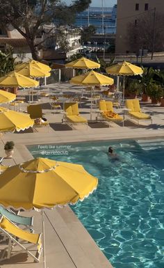 an empty swimming pool with yellow umbrellas and lounge chairs around the edge, in front of some buildings