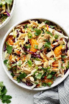 two white bowls filled with salad and garnished with cilantro, oranges, green onions