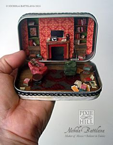 a hand holding a miniature model of a living room in a tin box with furniture inside