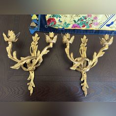 two golden wall sconces with floral designs on them sitting on a wooden floor