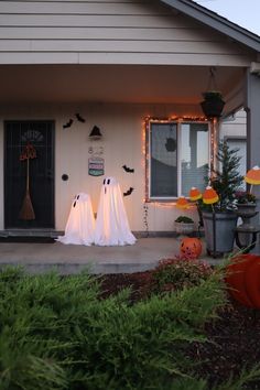 two ghost statues in front of a house decorated for halloween