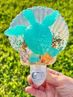 a hand holding up a blue and white fan with seashells on it in the grass