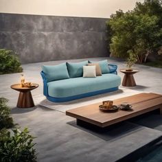 a blue couch sitting on top of a cement floor next to a table and potted plants