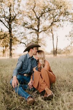 a man and woman are sitting in the grass together, one is wearing a cowboy hat