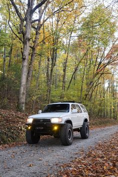 a white truck parked on the side of a dirt road in front of some trees