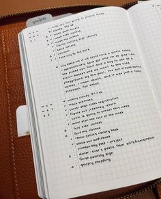 an open notebook with writing on it sitting in a brown leather case next to a pair of scissors